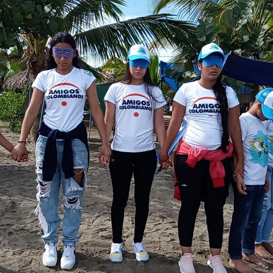 3 teenaged girls holding hands, getting ready to take off blindfolds to see their first glimpse of the ocean