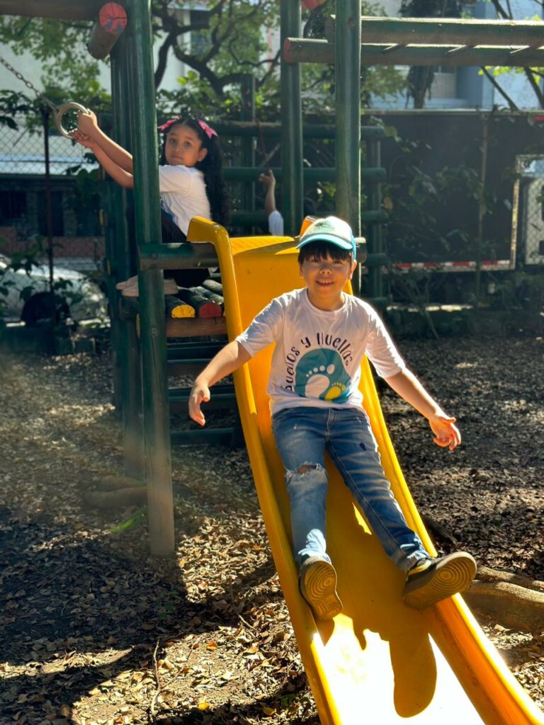 Boy at Casa de Sueños coming down a slide, smiling.