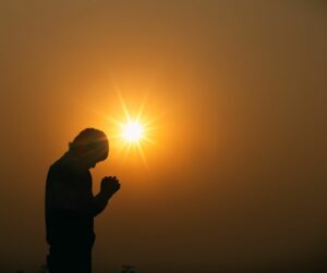 man praying under amber sun haze